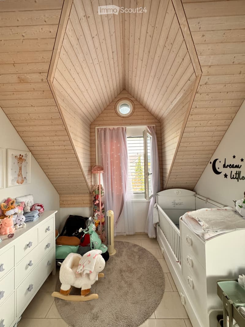 Cozy children's bedroom with wooden walls and slanted ceiling, featuring a bed, rocking horse, toy car, fan, and decorative elements.