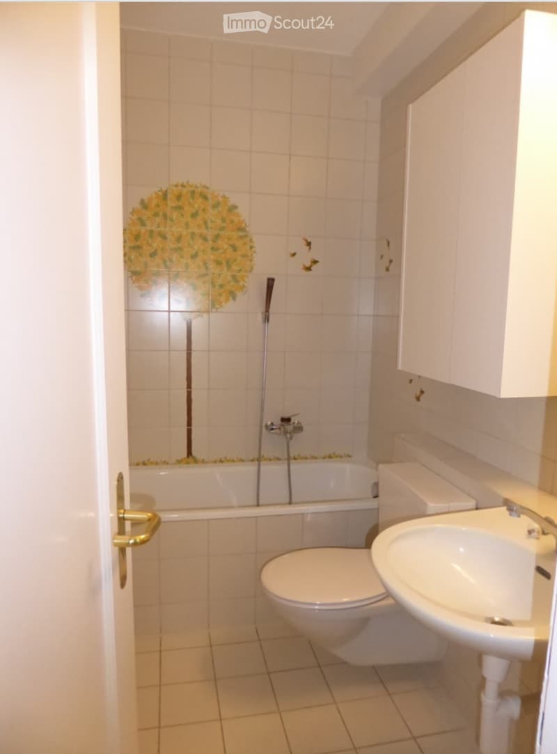 Bathroom with white tiles, a bathtub, toilet, sink, and a decorative tree design on the wall.