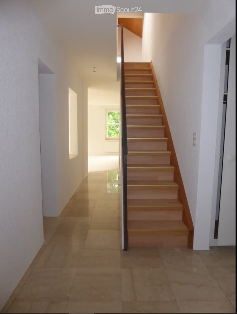 Modern hallway with tiled floor, white walls, and a wooden staircase with a metal railing leading upwards.