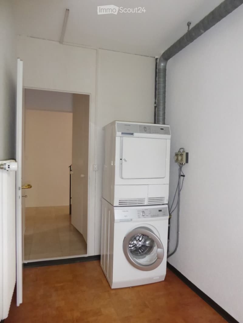 Bathroom with a stacked washing machine and dryer, wooden flooring, and white walls.