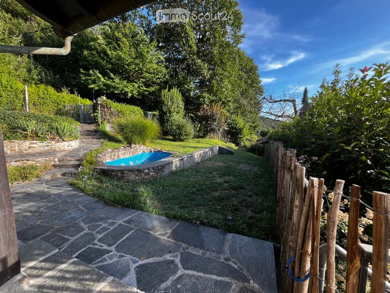 Garden with a stone pathway, small swimming pool, wooden fence, and lush greenery.