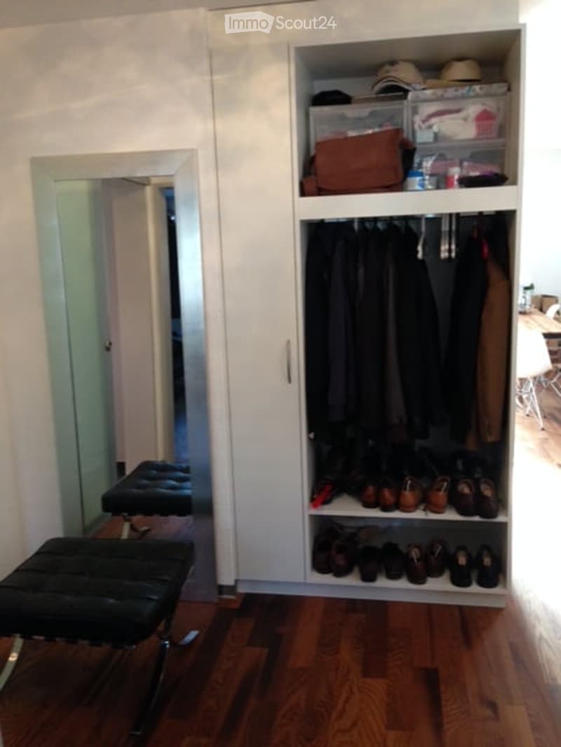 A well-organized walk-in closet with a large wardrobe, neatly arranged clothing, shoes, and accessories. A black leather stool sits in front of a full-length mirror.