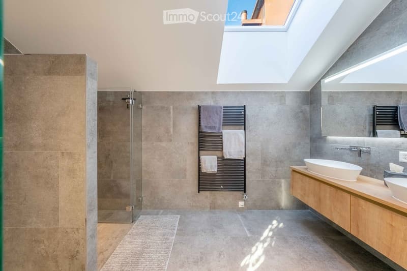 Modern bathroom with a large skylight, wooden vanity with two sinks, a towel rack with towels, and a glass-enclosed shower area.