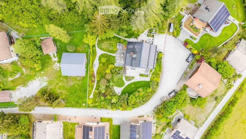 Aerial view of a residential area with multiple houses, green lawns, and parked cars.