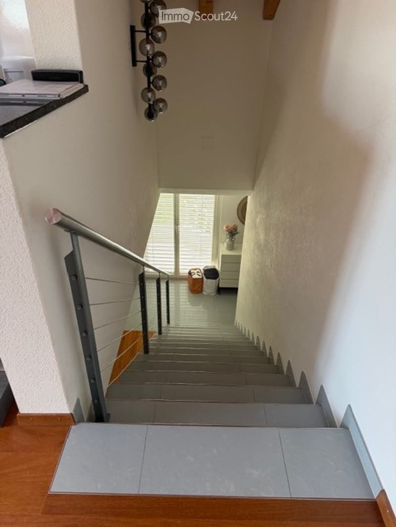 Modern staircase with metal railing and wooden steps, leading to an open area with a small table and vase.