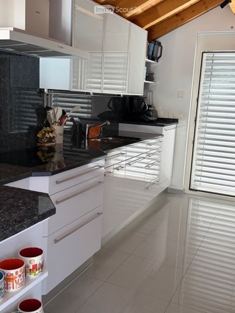 Modern kitchen with white cabinets, stainless steel appliances, granite countertops, and a large window with blinds.