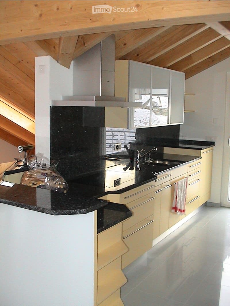 Modern kitchen with light-colored cabinets, black countertops, and stainless steel appliances. Features a sink, faucet, and oven.