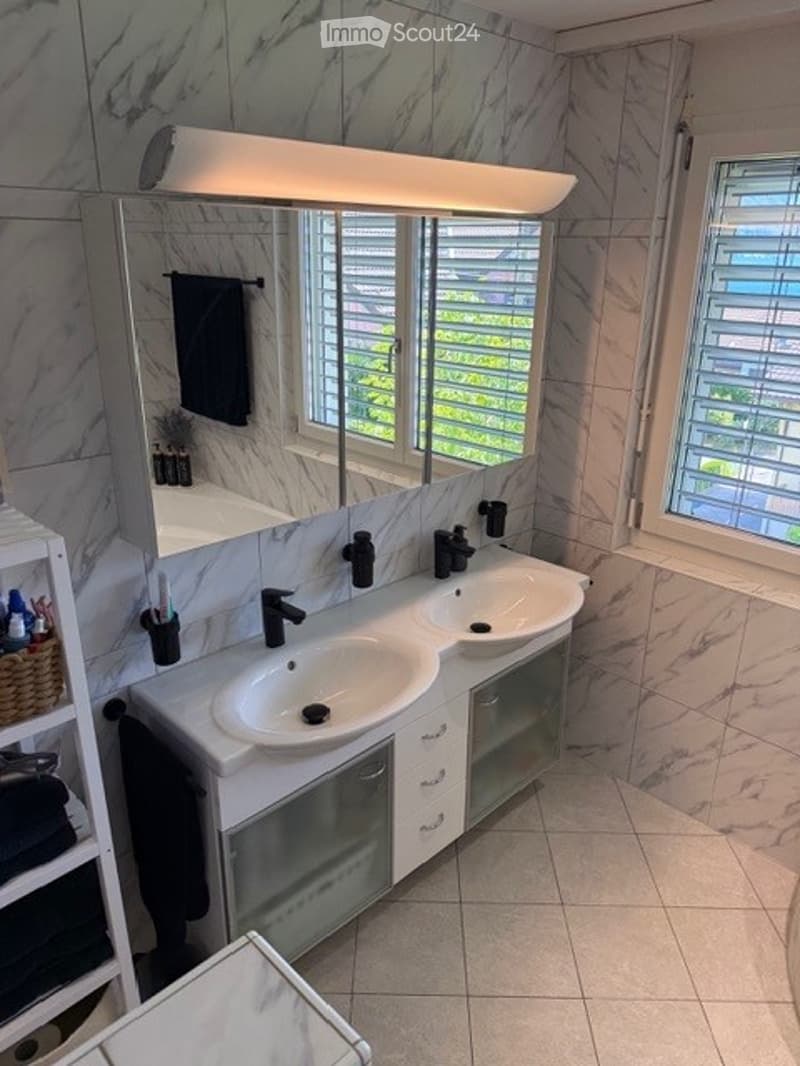 Modern bathroom with double sink vanity, marble tiles, large mirror, and natural light from windows.