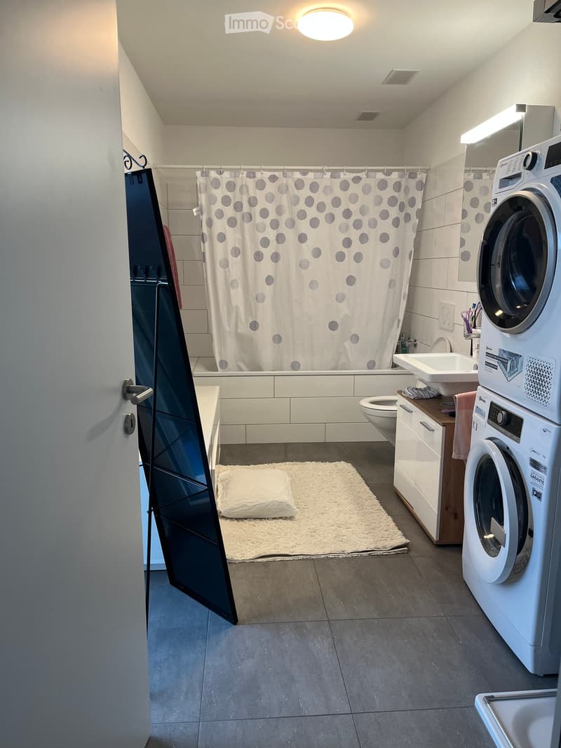 Modern bathroom with a bathtub, toilet, sink, washing machine, and a shower curtain with grey polka dots.