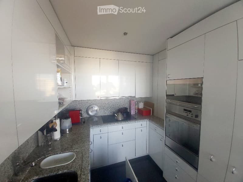 Modern kitchen with white cabinets, stainless steel oven, granite countertop, and various small appliances.