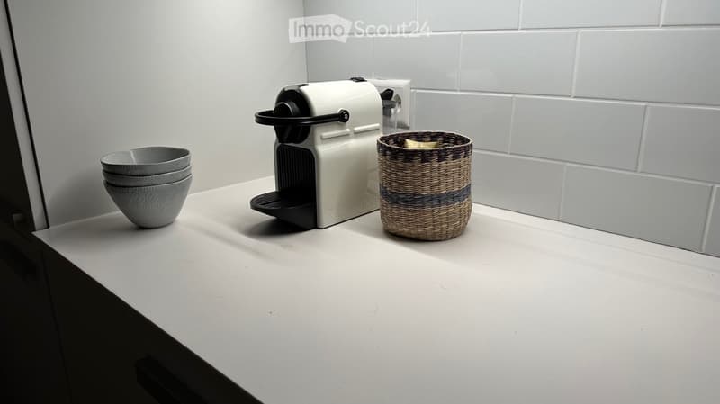 A modern kitchen countertop with a white Nespresso coffee machine, a woven wicker basket, and a stack of grey ceramic bowls.