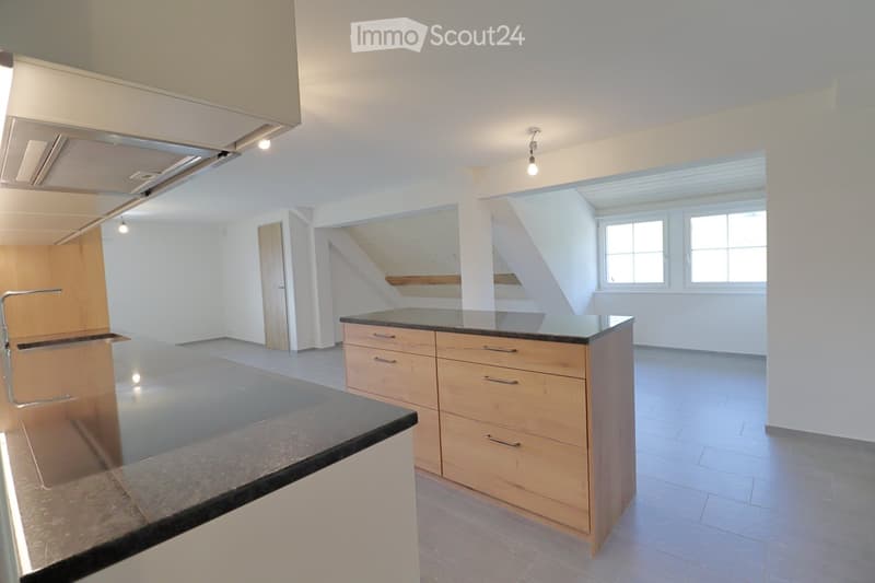 Modern kitchen with light wooden cabinets, a central island with a black countertop, and a stainless steel sink.