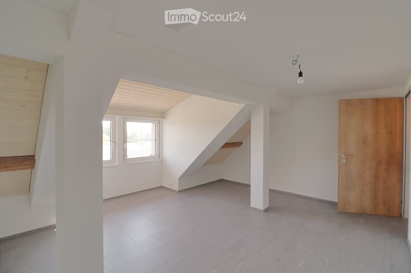 Empty room with white walls, grey tiled floor, wooden door, and a small staircase leading upwards.