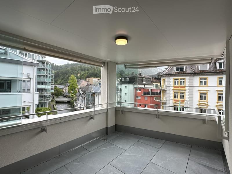 Modern balcony with tiled floor, glass railing, and a view of the city and surrounding landscape.