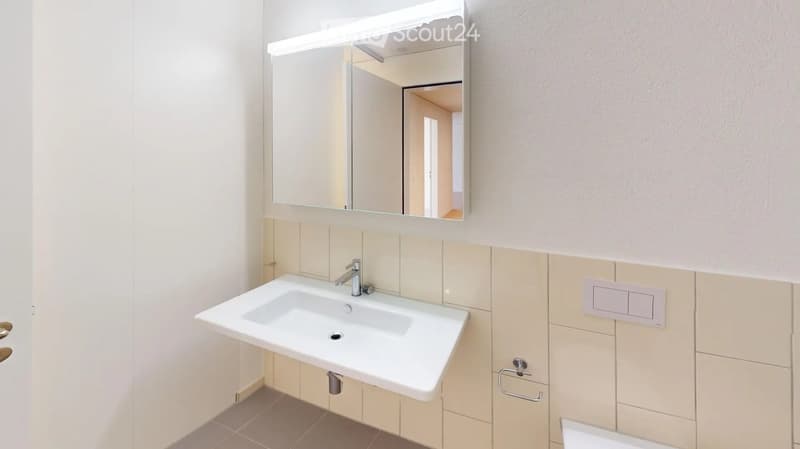 Modern bathroom with a white sink, chrome faucet, large mirror with built-in lighting, beige tiled walls, and a towel ring.