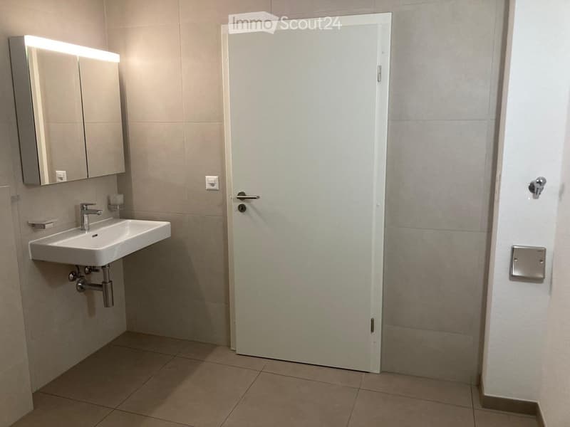 Modern bathroom with a white sink, mirror cabinet, and tiled walls and floor. A closed white door is visible.