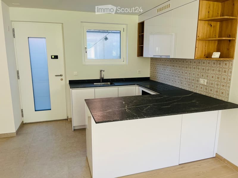Modern kitchen with white cabinets, black countertops, and a sink. Features a window and a door leading outside.
