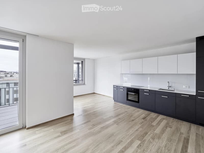 Modern kitchen with light wooden flooring, white walls, grey cabinets, and stainless steel appliances.