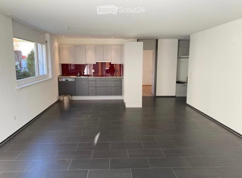 Modern kitchen with white cabinets, dark grey lower cabinets, and a dark tiled floor. Features a large window with a view of greenery outside.