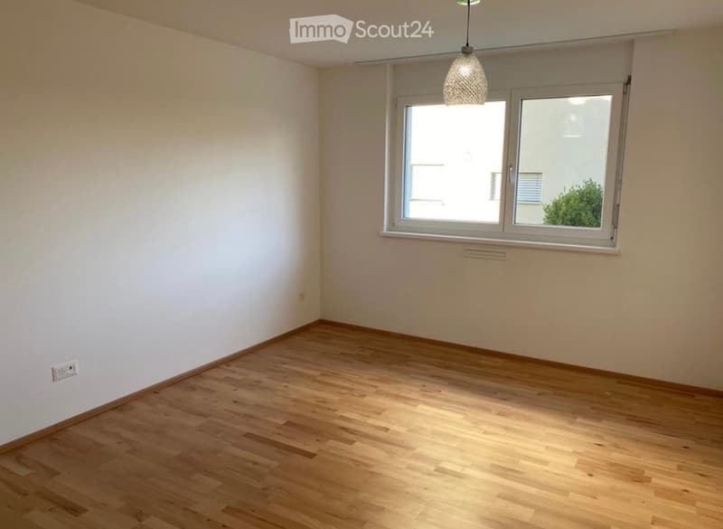 Empty room with wooden flooring, white walls, and a large window with a view of the outside.