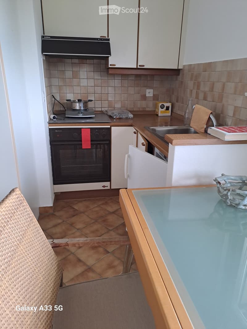 Compact kitchen with white cabinets, a stove, oven, sink, and a small dining table with a glass top.