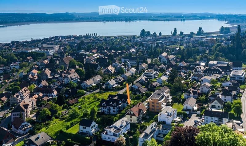 Aerial view of a residential neighborhood with numerous houses, surrounded by greenery and a body of water in the background.