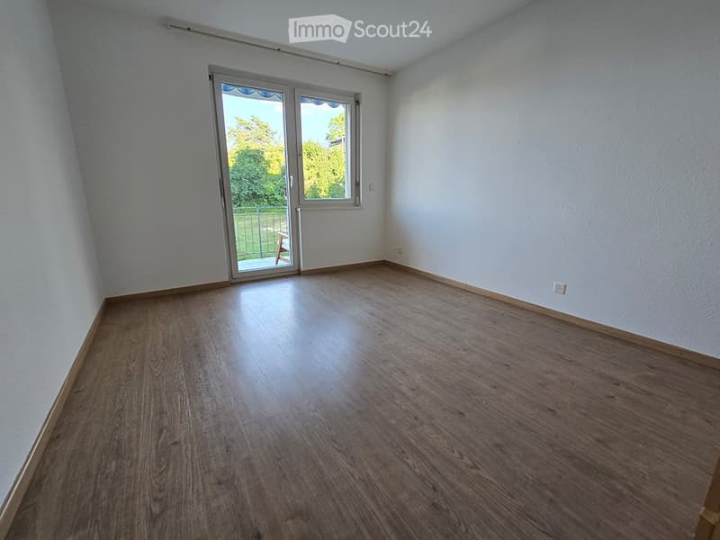 Empty room with wooden flooring, white walls, and a large sliding glass door leading to a balcony area.