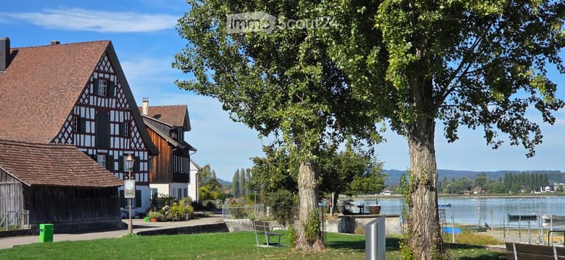 Traditional half-timbered house with a red-tiled roof, surrounded by greenery and a waterfront view.
