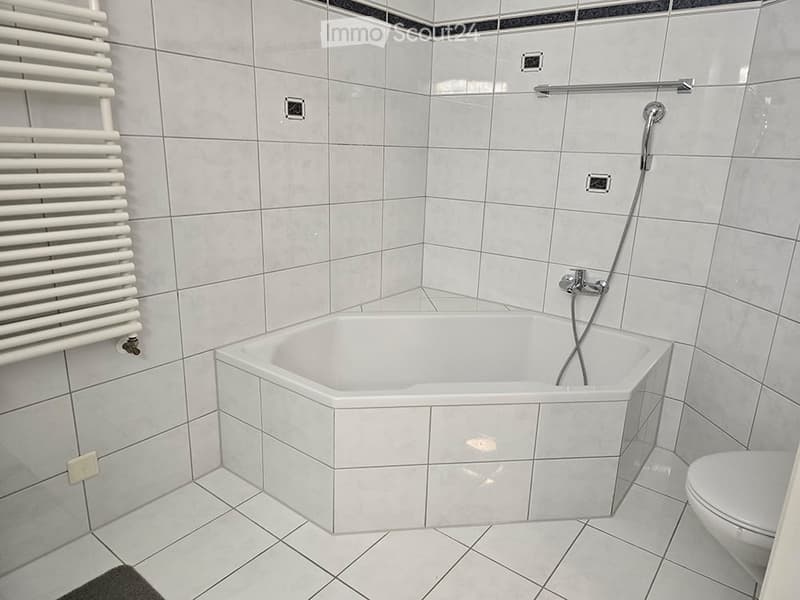 Modern bathroom with a white tiled bathtub, toilet, and a white radiator on the wall.
