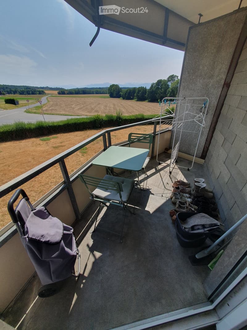 Balcony with a view of a rural landscape, featuring a small table, chairs, a baby stroller, and a laundry rack.