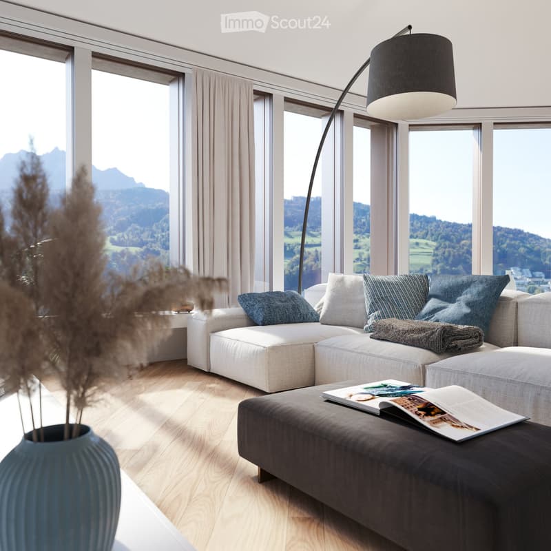 Modern living room with large windows offering a scenic mountain view, featuring a light-colored sectional sofa, a dark coffee table with magazines, a decorative vase with dried plants, and a floor lamp.