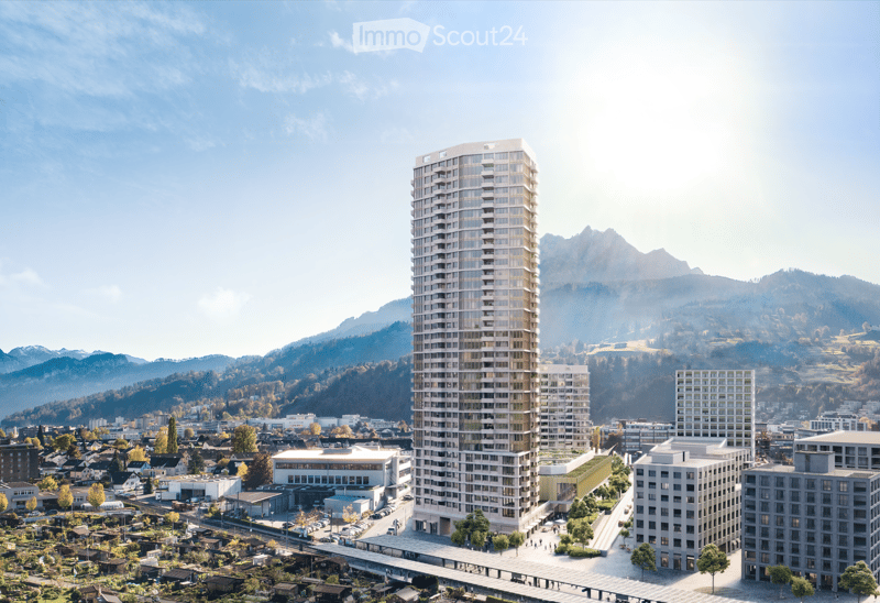A modern high-rise building with a sleek design, surrounded by smaller structures and a scenic mountainous backdrop.