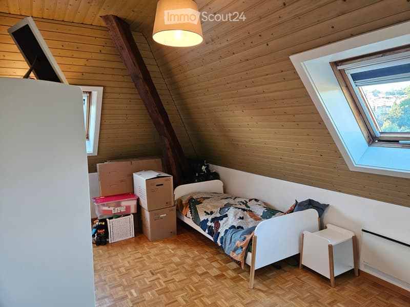 Cozy attic bedroom with wooden walls and slanted ceiling, featuring a single bed with a colorful blanket, a nightstand, storage boxes, and a wicker basket.