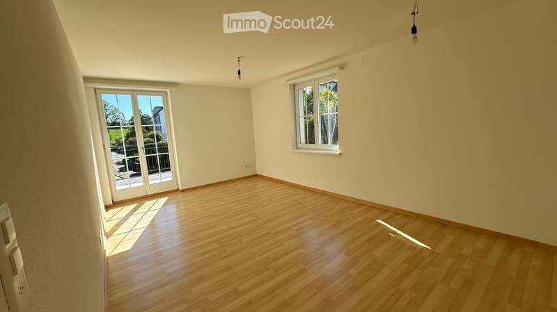 Empty room with wooden flooring, large windows, and a sliding glass door leading to a balcony.