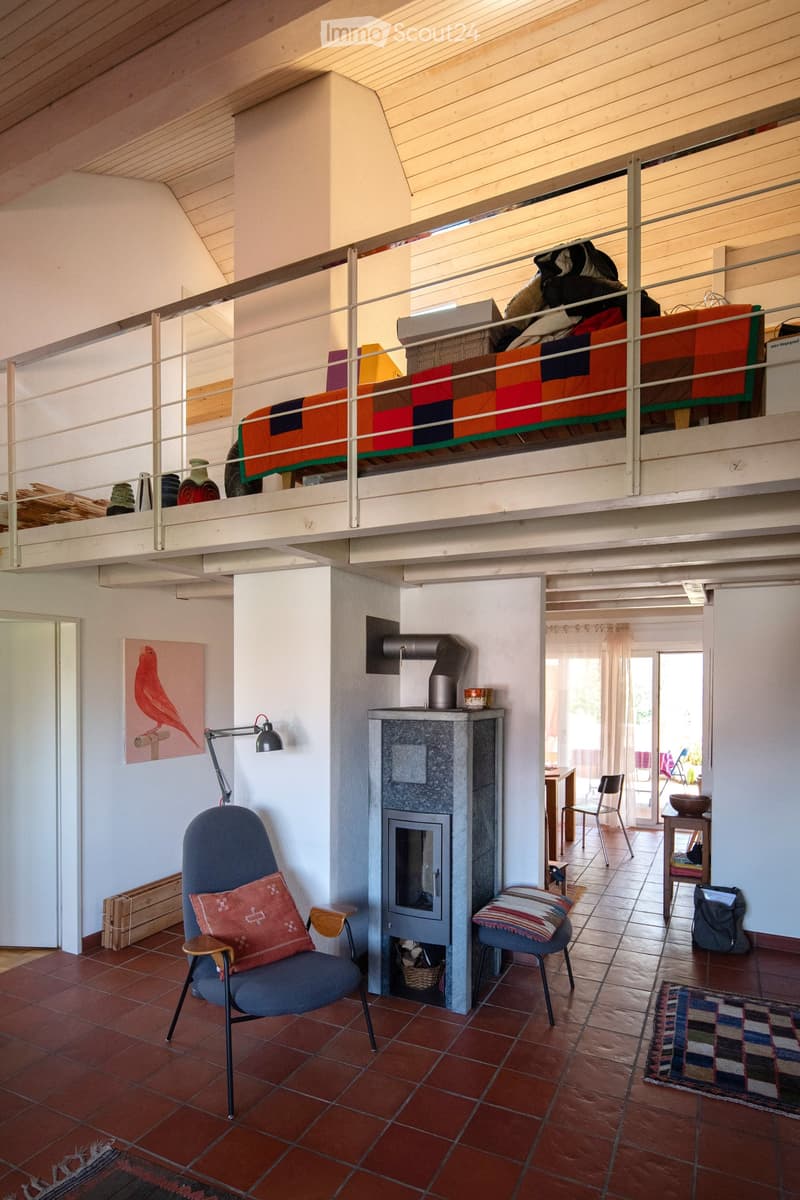 Open living space with a raised loft bed, fireplace, sofa, chairs, and artwork.
