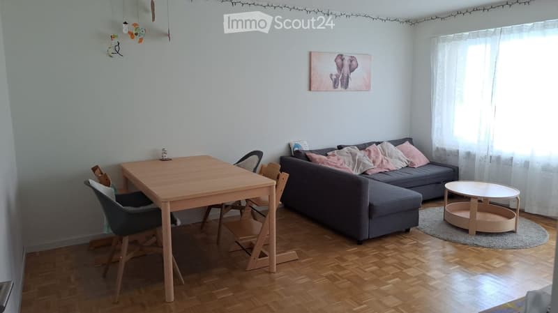 A modern living room with a grey sectional sofa, a wooden dining table with chairs, a small round coffee table, and a painting on the wall.