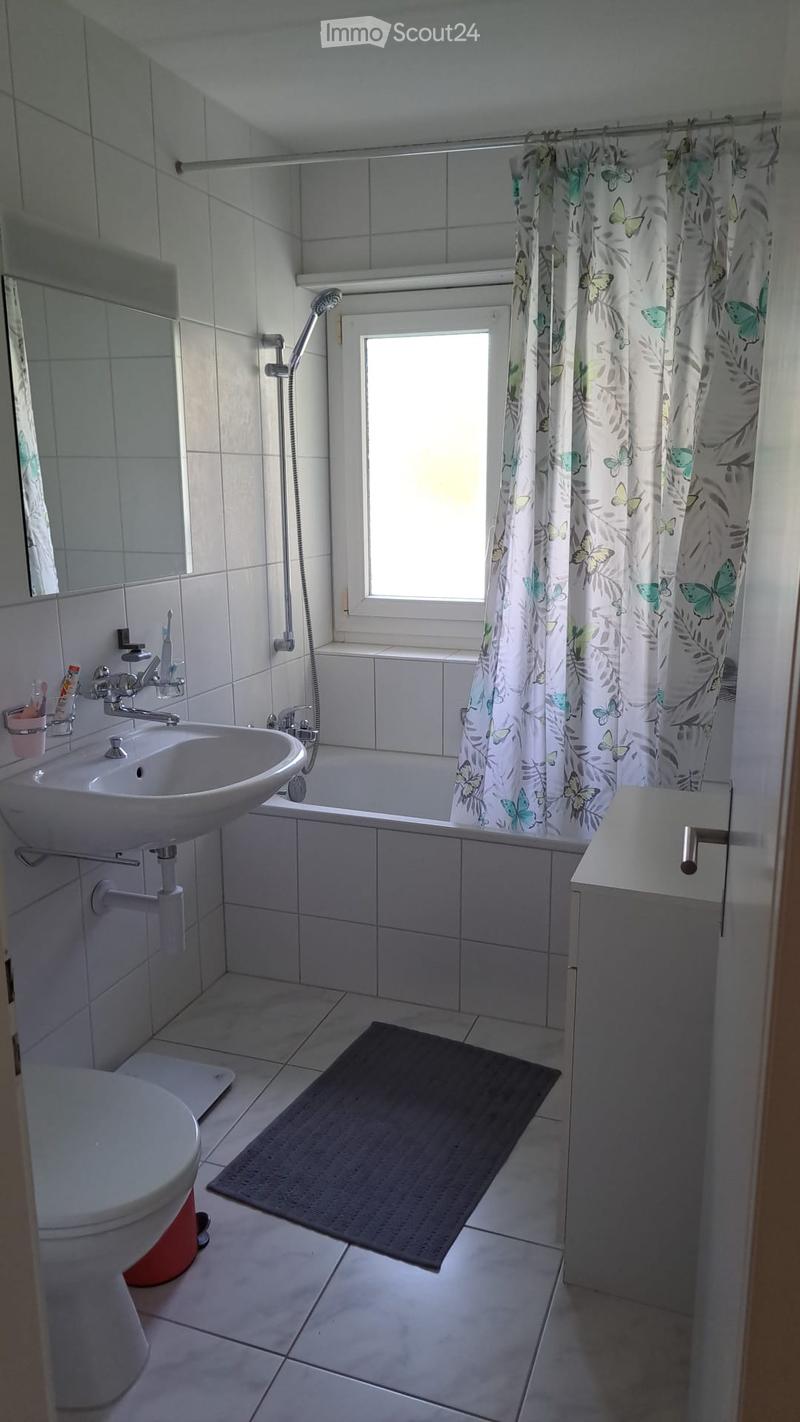 Modern bathroom with white tiles, a bathtub, a sink, a toilet, a shower, and a decorative shower curtain with butterfly patterns. A small rug is placed in front of the bathtub.