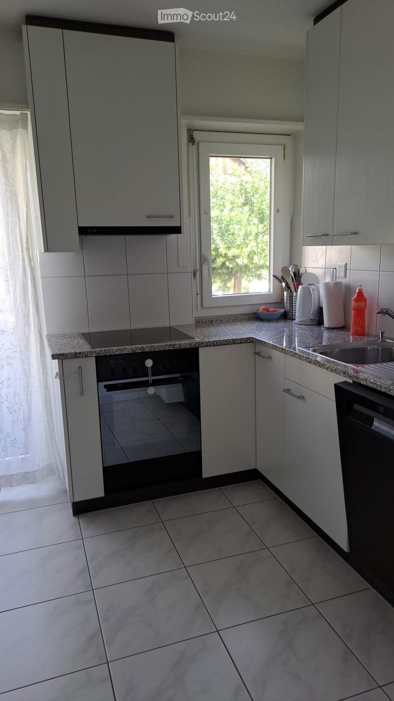Modern kitchen with white cabinets, granite countertops, and stainless steel appliances including an oven, sink, and dishwasher. A window with a curtain lets in natural light.