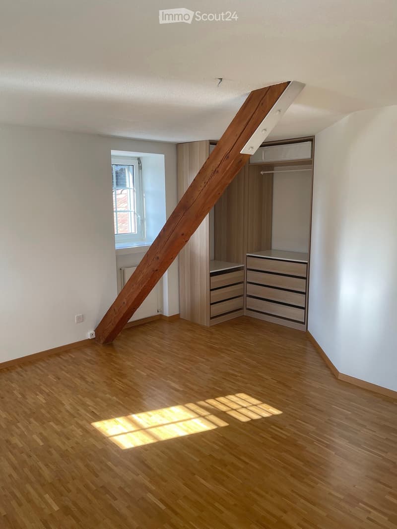 Empty room with wooden flooring, white walls, built-in closet with drawers, and a window letting in natural light.