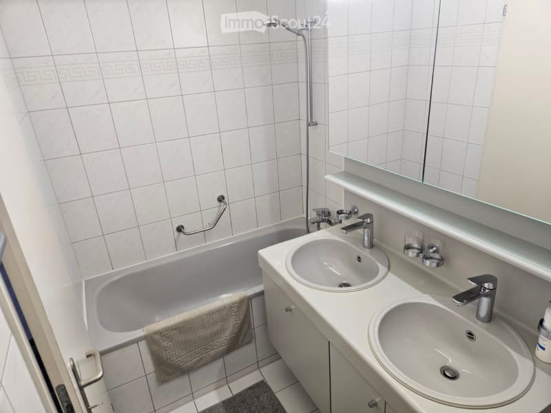 Modern bathroom with white tiles, a bathtub, double sink, and a large mirror above the sink.