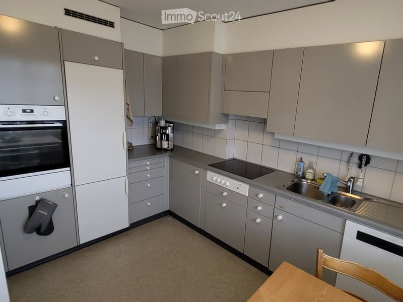 Modern kitchen with grey cabinets, stainless steel appliances, and a wooden dining table with a chair.