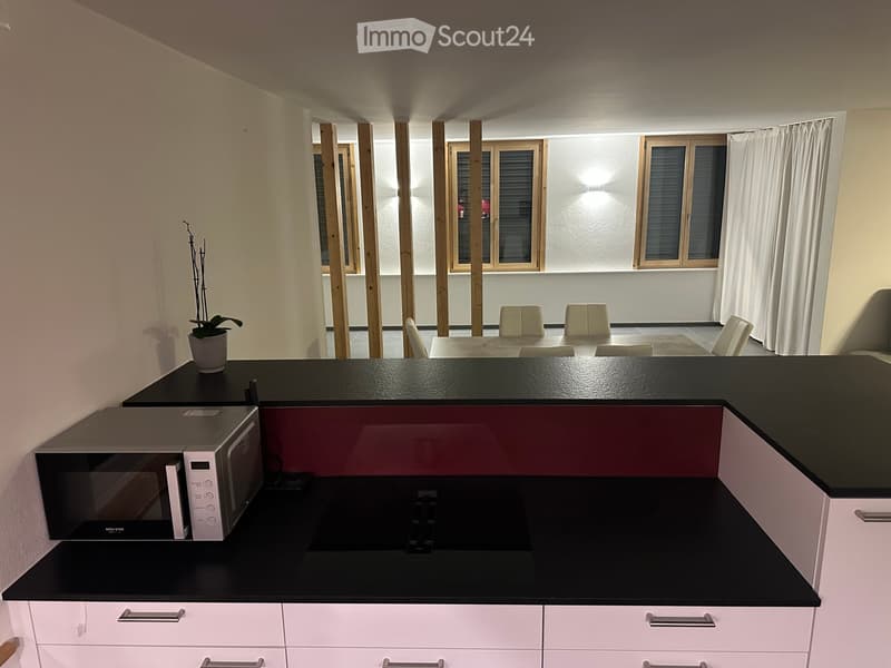 Modern kitchen with white cabinets, black countertops, microwave, and a small dining area with chairs and a table.