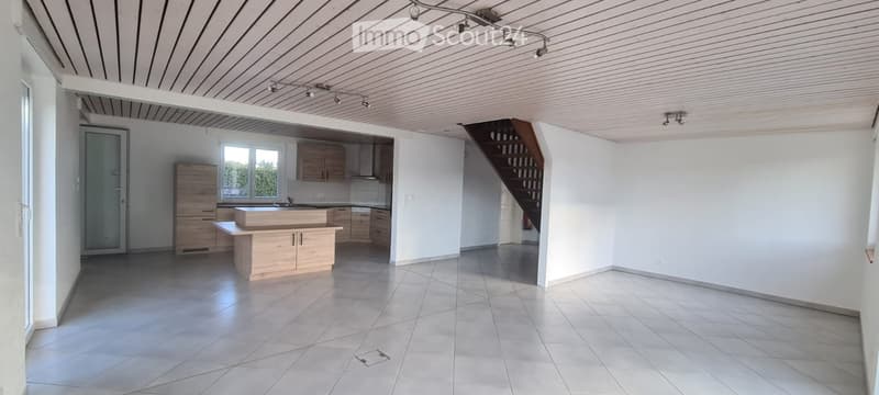 Open-plan kitchen and living area with light wooden cabinets, a central kitchen island, and tiled flooring.