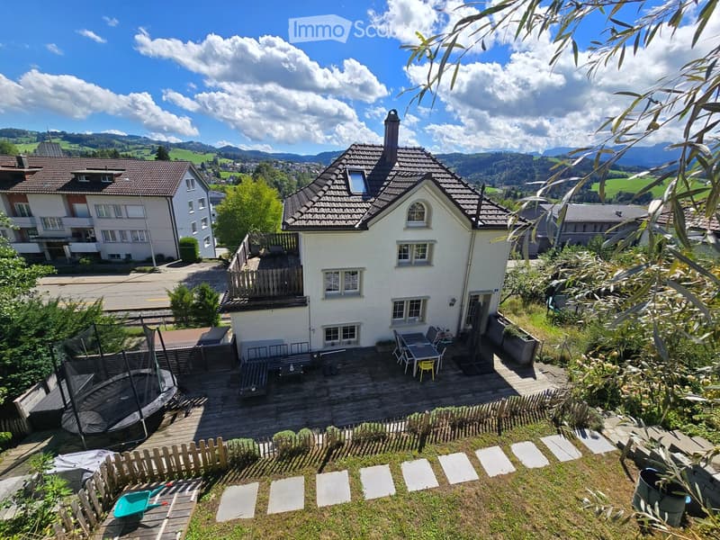A peaceful garden and outdoor area with a trampoline, patio furniture, and a scenic mountain view in the background.