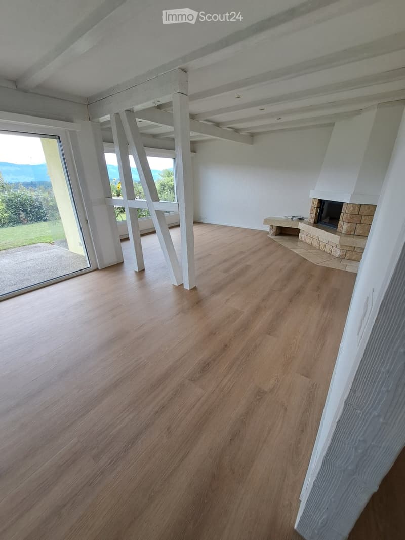 Modern living room with wooden flooring, large windows offering a scenic view, and a stone fireplace.