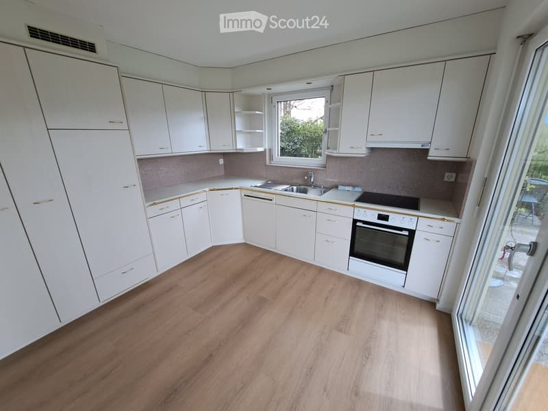 Modern kitchen with white cabinets, wooden flooring, and stainless steel appliances including a sink, stove, and oven.