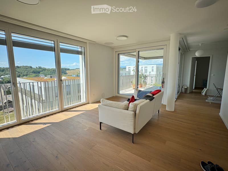 Bright living room with wooden flooring, large windows, and a balcony overlooking a scenic view.