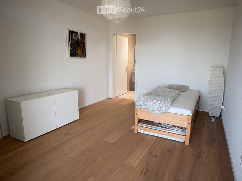 Minimalist bedroom with wooden flooring, a single bed with a blanket, a white cabinet, and a picture frame on the wall.