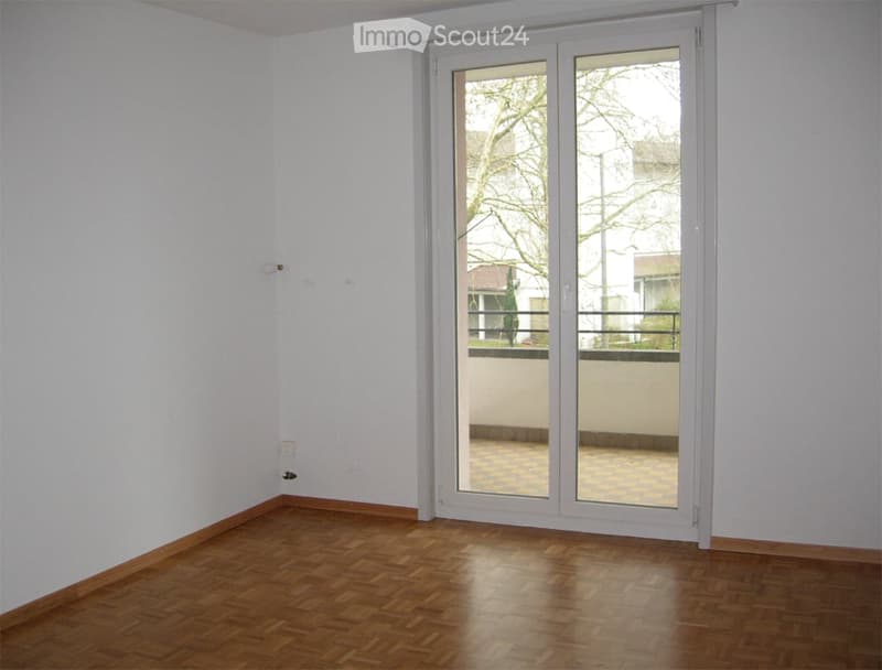 Empty room with wooden flooring, white walls, and a large sliding glass door leading to a balcony.