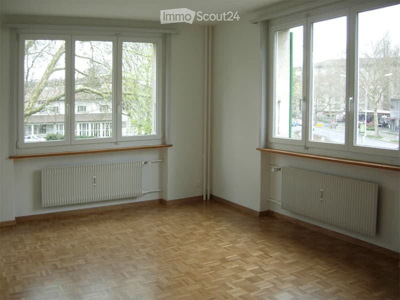 Empty room with wooden flooring, large windows, radiators, and wooden window sills.